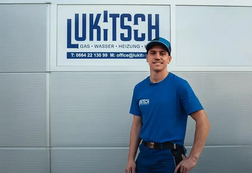 Monteur mit Kappe vor dem Firmenschild LUKITSCH Gas, Wasser, Heizung an der Fassade