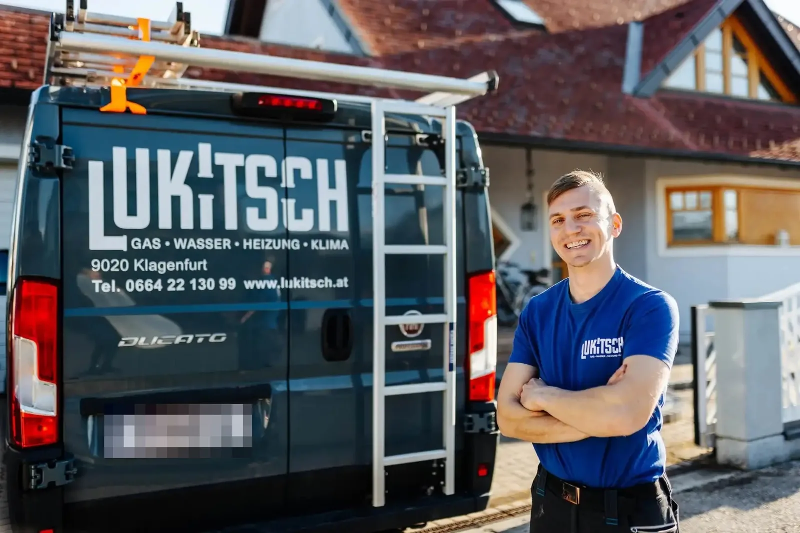 Monteur im blauen Lukitsch-Shirt vor dem beschrifteten Firmenwagen