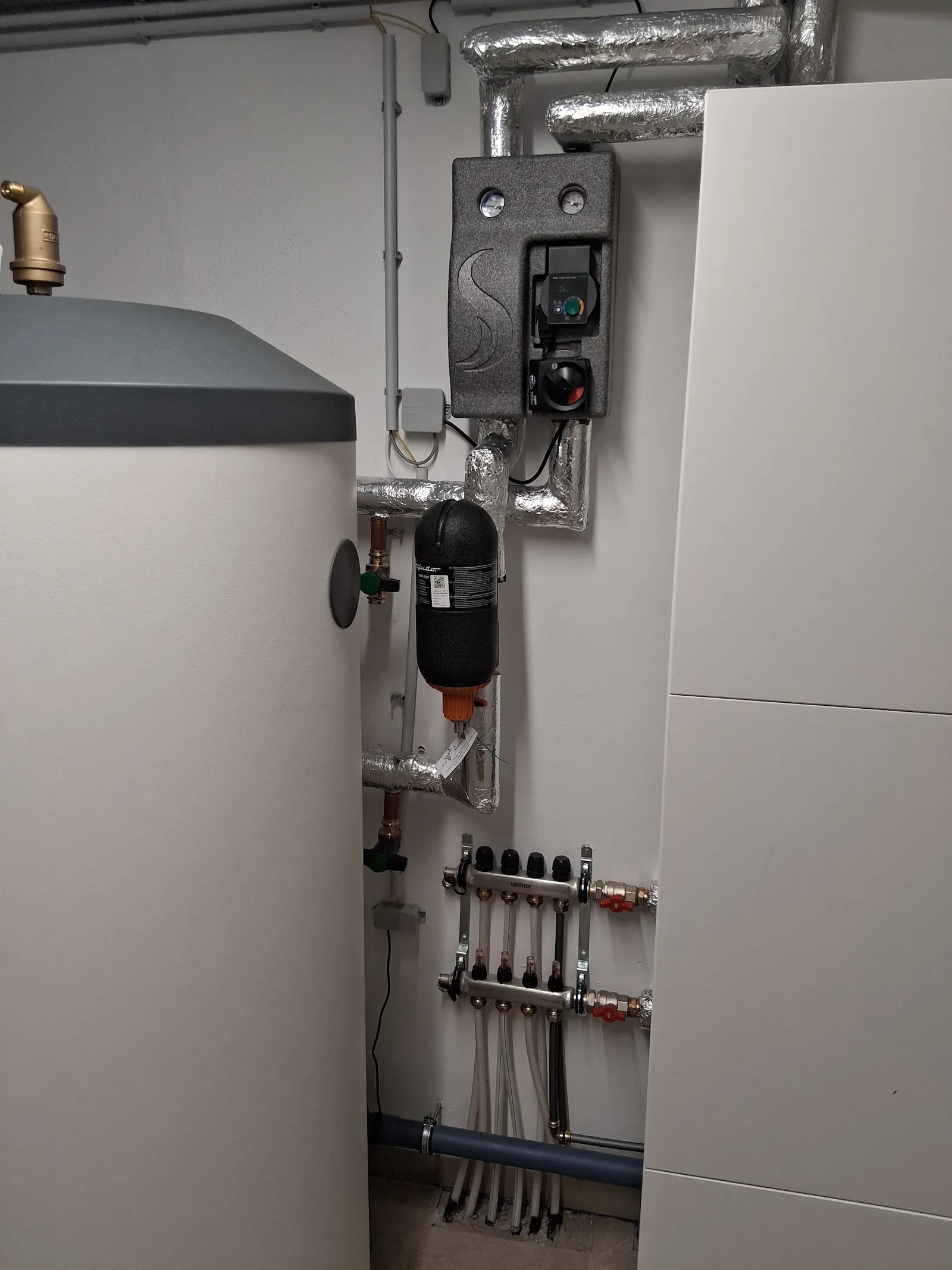 Speicher, Pumpengruppe und Heizkreisverteiler an der Wand des Heizraums